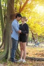 Romantic young couple standing under big tree while embracing on sunset in the park. Cheerful man hugging his girlfriend feelings Royalty Free Stock Photo