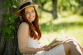 Romantic young lady in straw hat reading a book sitting in garden.