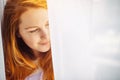 Romantic young redhead girl with long hair, close-up, copy space. Portrait of beautiful smiling woman with perfect skin on light Royalty Free Stock Photo