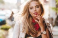 Romantic young woman with red manicure posing in sunny town after work. Close-up portrait of enchanting blonde lady in