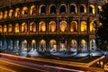 Rome Colosseum by night with yellow lighted archs and long exposured car lights.