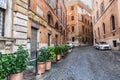 Rome, Italy - August 22, 2018: Typical old Roman narrow street. Green plants in front of small restaurant windows.