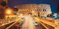 Rome, Italy. Colosseum Also Known As Flavian Amphitheatre In Evening Or Night Time. Night Traffic Light Trails Near