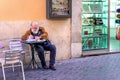 Rome, Italy - December 17, 2019: Elderly senior Italian man in reading newspaper in street cafe in historic city