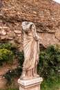 Ancient headless statue near brick wall and green plants