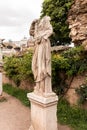 Ancient headless statue near old wall and green plants