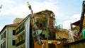 Demolition of a building with the aid of a crane with gripper, and water jet seen from below, in a Roman district