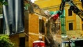 Demolition of a building with the aid of a crane with gripper, and water jet seen from below, in a Roman district