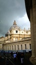 St. Peter`s Square with Bernini`s colonnade on the sides, with Latin inscriptions on the facade and large antique clock on a cloud