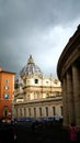 St. Peter`s Square with Bernini`s colonnade on the sides, with Latin inscriptions on the facade and large antique clock on a cloud