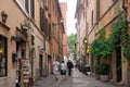 People walk along Via della Lungaretta, a picturesque cobblestone street lined with old buildings and quaint shops in Rome, Italy.