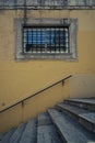 Stone window with metal bars, in a yellow wall with stairs underneath Royalty Free Stock Photo