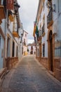 RONDA, SPAIN - FEBRUARY 03, 2014: Narrow cobble stone paved street with traditional andalusian white houses and flags in pueblo b