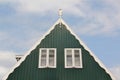 Roof detail of an Holland wooden house in green color with two white windows on a blue sky. Royalty Free Stock Photo