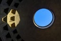 Roof of the dome of the pantheon in Rome seen from the inside with circular hole in the blue sky and light projected on top.