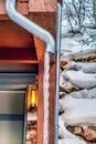 Roof drain pipe of home with frozen water against snowy and rocky hill slope Royalty Free Stock Photo