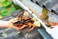 Roof gutter cleaning in autumn. A house owner is cleaning a rain gutter by removing fallen leaves with hand from the roof gutter Royalty Free Stock Photo