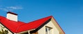 Roof of a house or cottage made of red metal tiles with drains, slopes, tides, chimney against the blue sky. Metal roof for roof