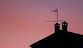 Roof of a house, fireplaces and antenna at sunset.