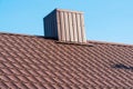 The roof of a house with modern metal tiles and a chimney, against the background of a blue sky. Metal roofing Royalty Free Stock Photo