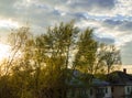 Roof of the old house behind trees against cloudy sky with clouds and sunset Royalty Free Stock Photo