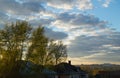 Roof of the old house behind trees against cloudy sky with clouds and sunset Royalty Free Stock Photo