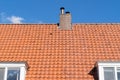 A Roof with red roof tiles and chimney and a clear blue sky with some clouds on a sunny day Royalty Free Stock Photo