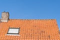 A Roof with red roof tiles, a window and chimney and a clear blue sky with some clouds on a sunny day Royalty Free Stock Photo
