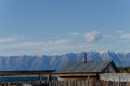 The roof of a small wooden house on the banks of the river against the backdrop of mountains and blue sky. Royalty Free Stock Photo