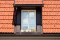 Roof window with white wooden frame covered with new roof tiles and with four glass containers filled with organic homegrown herbs