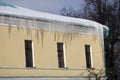 The roof of a yellow county house is covered by icicles.