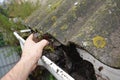 Roofer cleaning with hand roof gutter from fallen leaves and dirt in fall