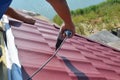 Roofer contractor installing metal roof tile with screwdriver.