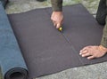 Roofer cutting roll roofing felt or bitumen during waterproofing works.