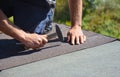 Roofer installing asphalt shingles on house construction roof corner with hammer and nails. Roofing construction.