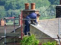 Roofer repairing chimney on slate roof in rural setting.