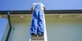 Roofer repairing the house roof. Roofer at work. Roofer standing on the metal ladder. Royalty Free Stock Photo