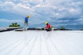 .Roofer using electric drill nail gun installing Roof sheet under construction. Construction worker wearing safety harness belt