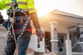 A Roofer wearing safety harness belt stands holding an air gun or pneumatic nail gun. the front of the building on the