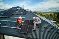 Men workers installing solar panels on roof of house.
