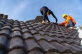 2 roofers working on the working at height to install the Concrete Roof Tiles on the new roof of new modern building construction