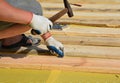 A roofing contractor is installing wooden sheathing, deck, planks on a vapor barrier membrane using a hammer and nails while metal