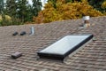 Rooftop view of residential asphalt shingle roof, skylight, roof vents, fall foliage in background