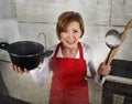 Rookie home cook woman in red apron at home kitchen holding cooking pan and rolling pin crying sad in stress