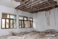 Room in abandoned building with broken windows and hanging ceiling insulation