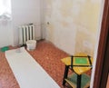 A room with bare walls and papered wallpaper. The roll of wallpaper is on the floor and the glue is in the bucket.