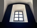 The room is in black and white with thick walls and one closed window with bars. Interior of an old building with arched window