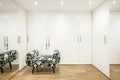 Room dedicated to a walk-in closet with smooth white wooden doors and large mirrors, wooden flooring and an upholstered armchair Royalty Free Stock Photo