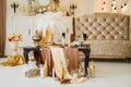 The room has a large sofa, next to it is a table with a festive serving of plates, wine glasses, feathers. On the floor are golden