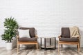 Room interior with modern armchairs and table near brick wall